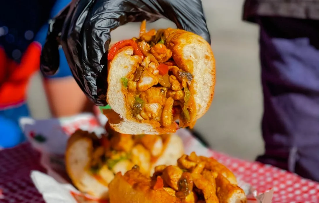 Gloved hand holding a messy sandwich loaded with chunky nuts and sauce