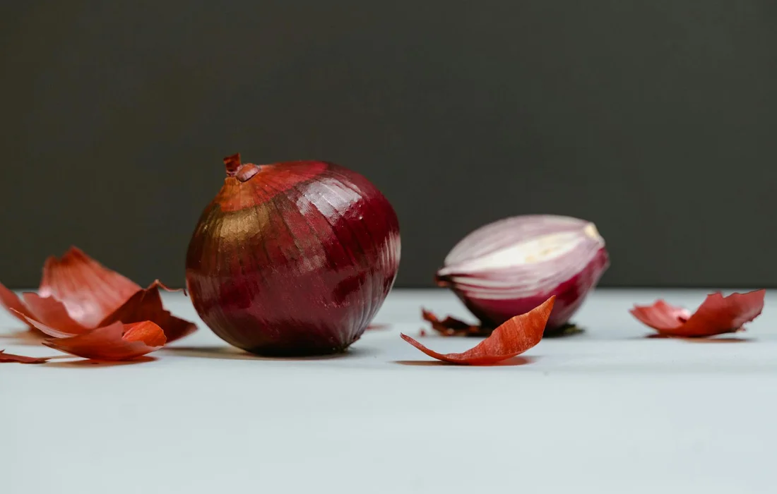 Close-up of red onions with scattered onion peels on a light surface