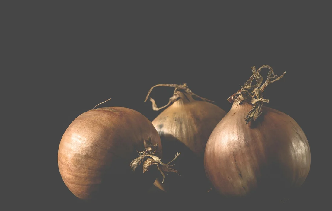 Three brown onions on a dark gray background