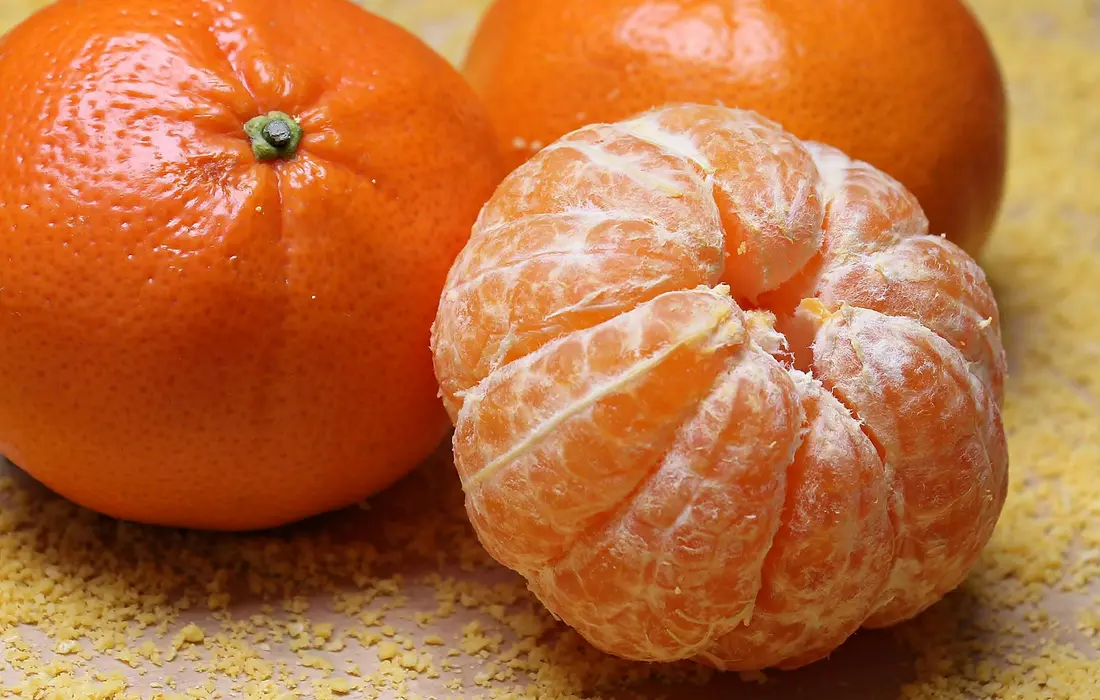 Close-up of fresh oranges, one peeled, on a textured yellow surface