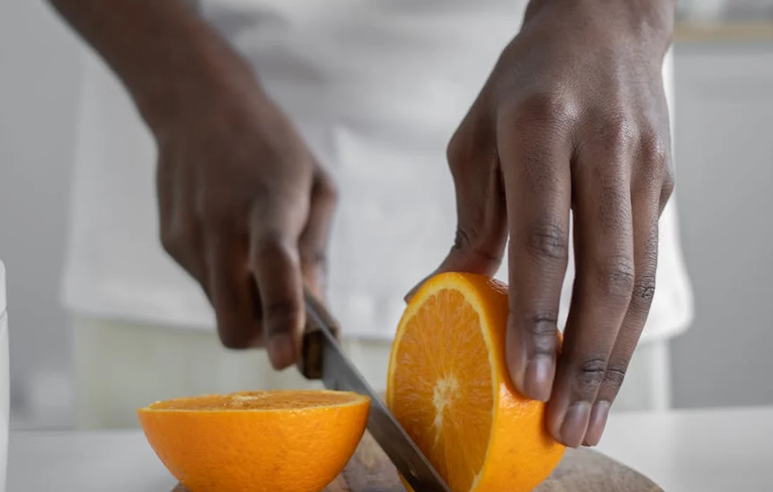 Close-up of hands slicing an orange on a cutting board.
