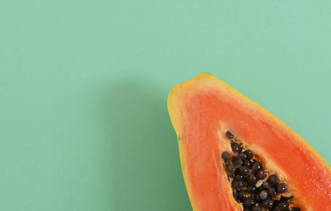 A fresh papaya wedge with seeds on a light green background