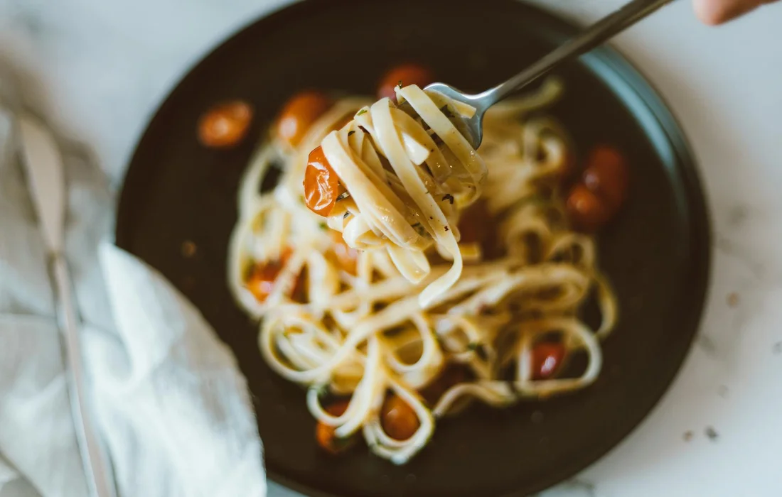 Plate of spaghetti with cherry tomatoes on a dark plate, with a fork lifting a strand of pasta.