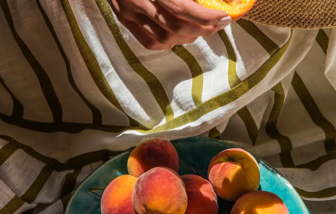 A person holds a peach above a plate of peaches, highlighting peach fruit and the importance of proper preparation when feeding rabbits.