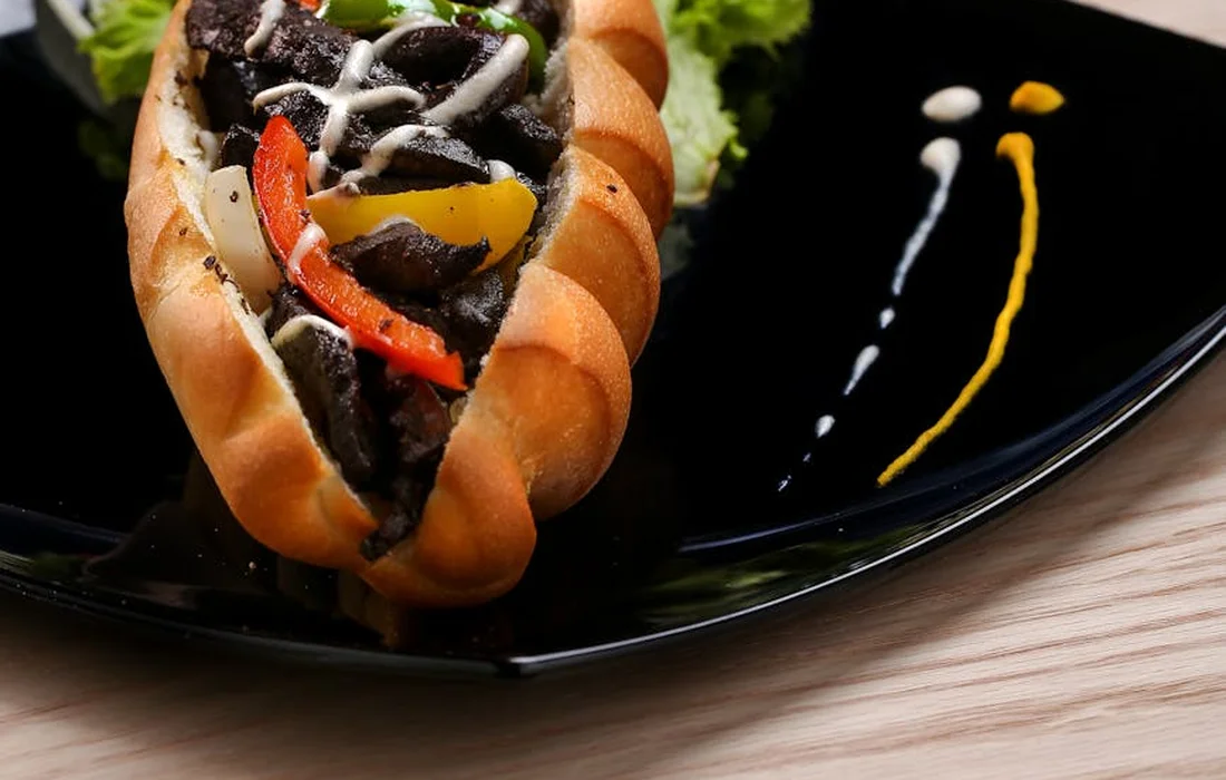 A colorful stuffed pepper served in a warm bun on a black plate, with decorative sauce streaks.