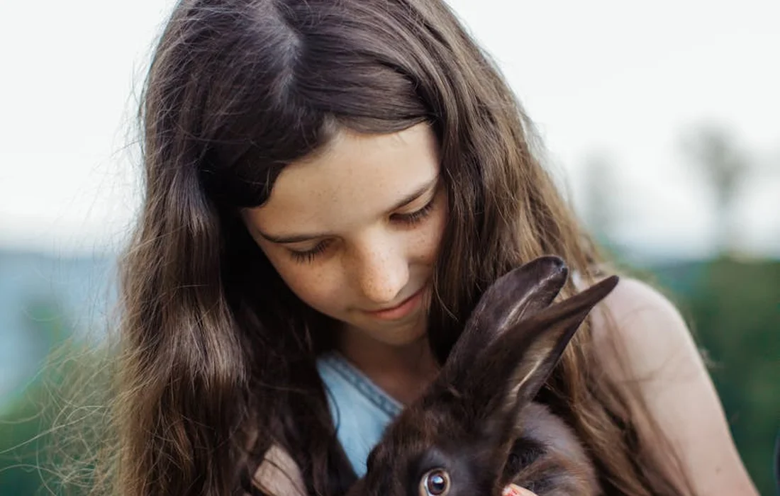Person holding a brown rabbit outdoors with a calm, attentive expression.