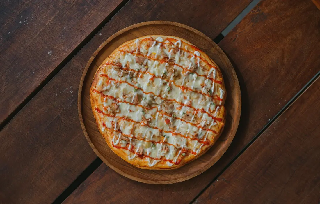A cheese pizza on a round wooden board placed on a dark wooden table.