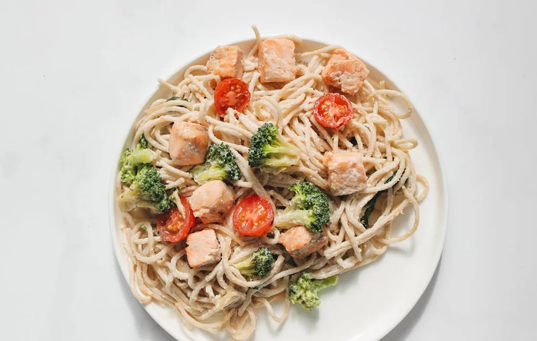Plate of spaghetti with broccoli florets and diced meat on a white plate