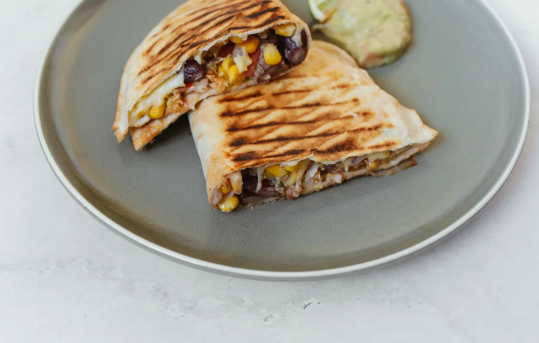 A gray plate with a grilled wrap cut in half, revealing corn kernels and black beans inside.