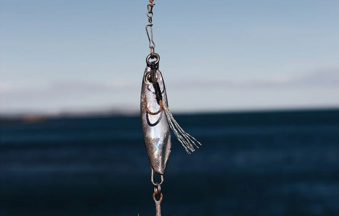 A fishing lure hanging from a line above a blurred blue pond.