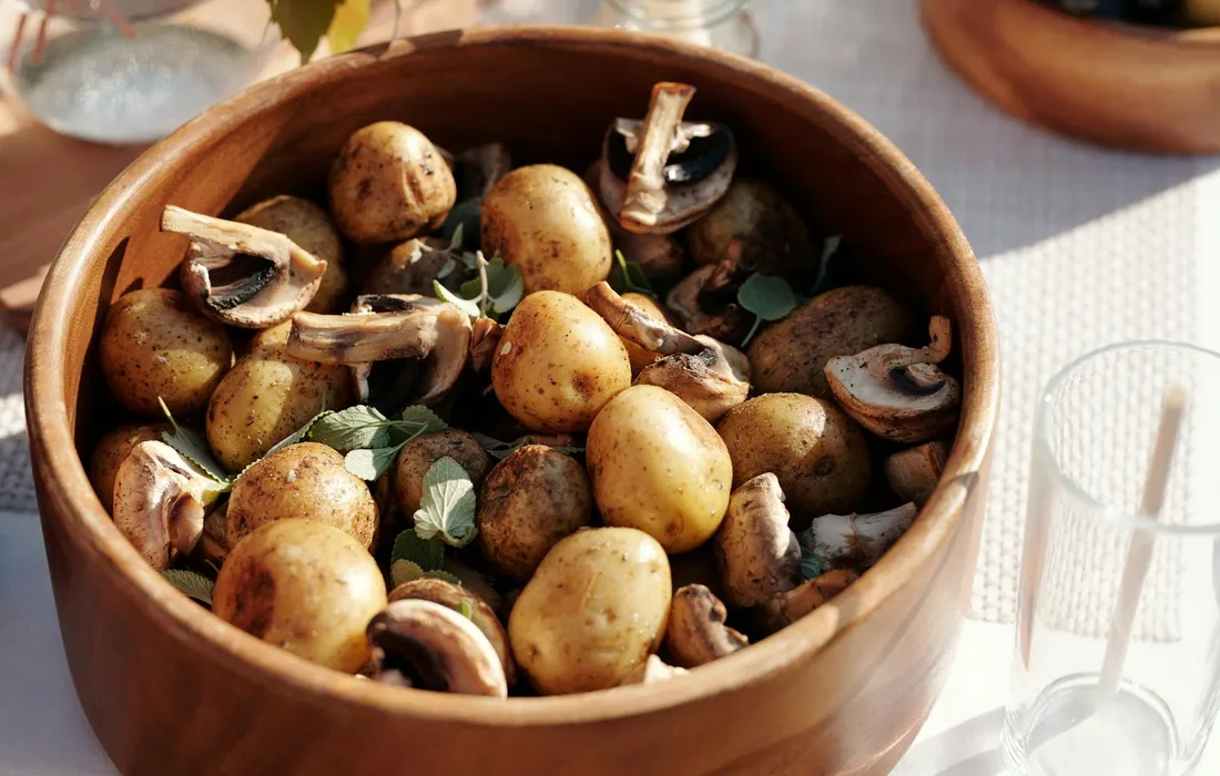 Wooden bowl filled with small potatoes and a few mushroom pieces, ready to be prepared for cooking.