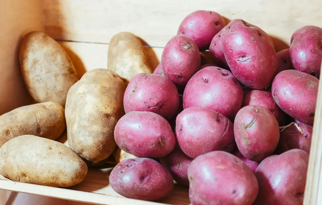 A collection of red-skinned and brown potatoes in a wooden crate.