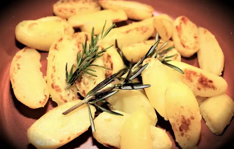 Sliced potatoes browning in a skillet with a sprig of rosemary