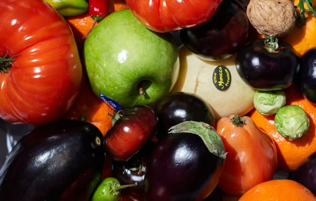 Assorted fresh produce, including tomatoes, eggplants, peppers, and a green apple, laid out together.