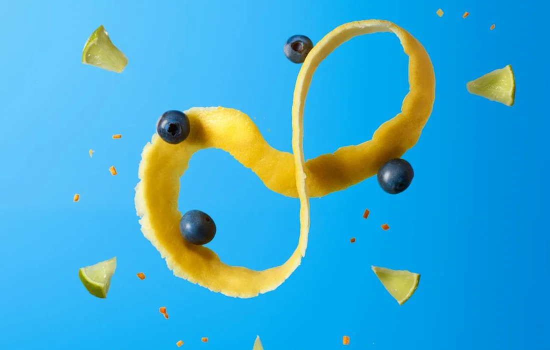 Blueberries placed on a curved yellow banana peel against a bright blue background.