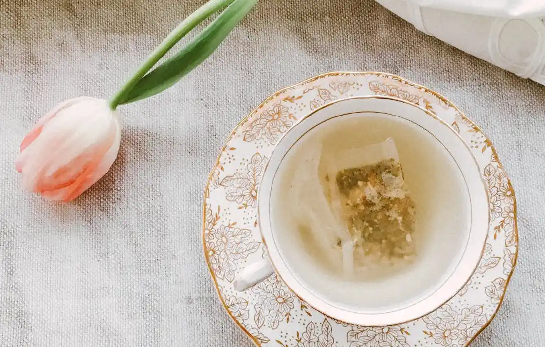 A pink tulip rests beside a decorative teacup on a light textured tablecloth, a still-life image for garden planning.