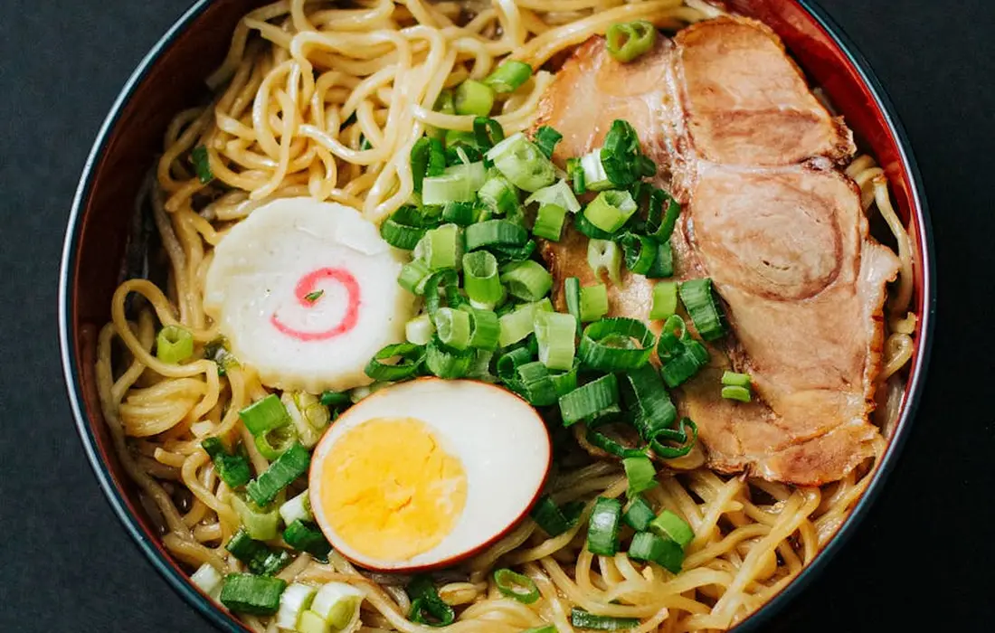 A bowl of ramen topped with sliced pork, a halved boiled egg, chopped green onions, and narutomaki on a bed of noodles.