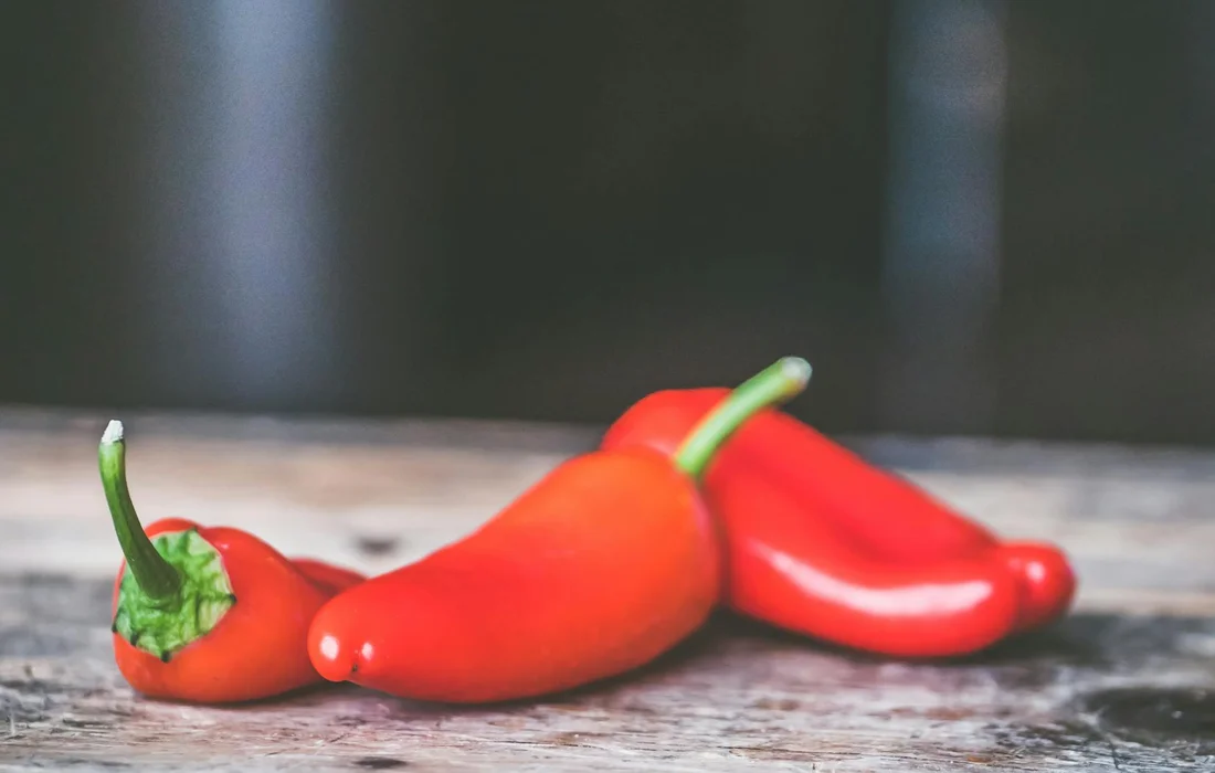 Three red bell peppers on a rustic wooden surface, representing cautions about feeding peppers to rabbits.