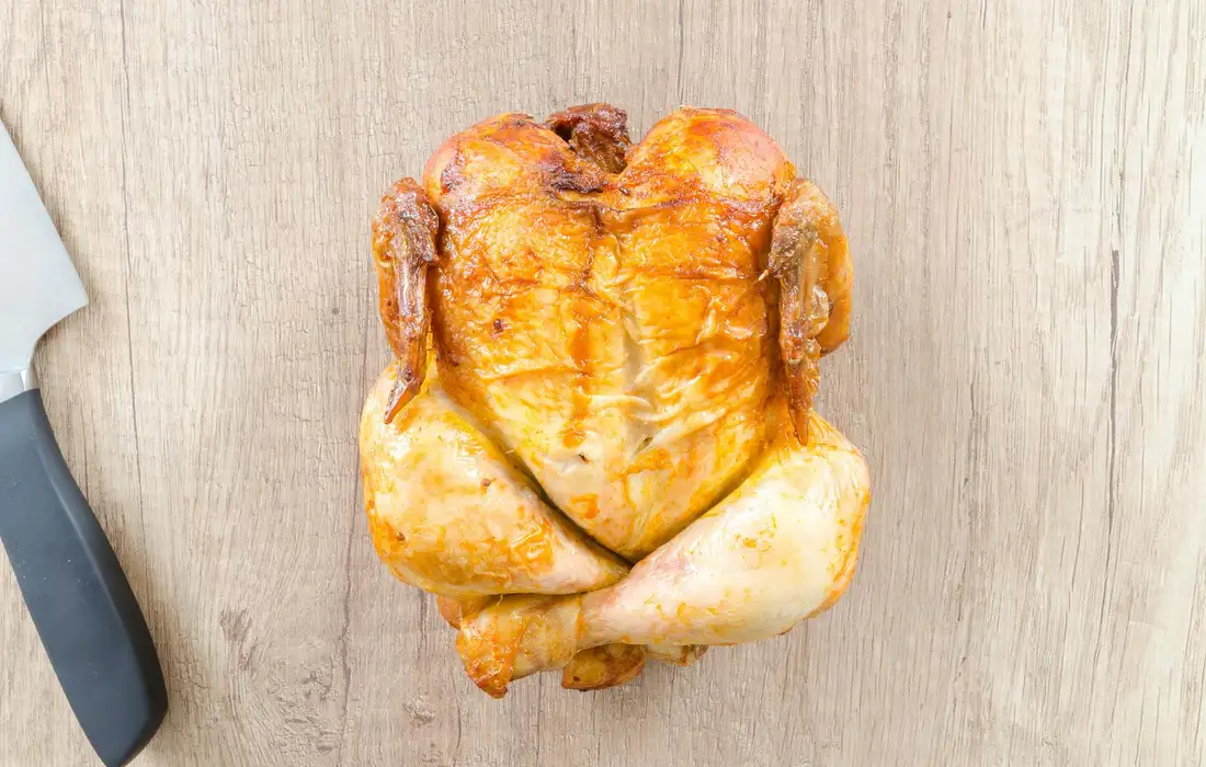Roasted chicken leg resting on a wooden cutting board with a kitchen knife nearby