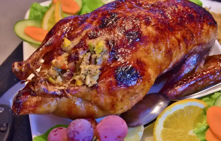 A roasted whole chicken on a platter with lemon slices, grapes, and vegetables.