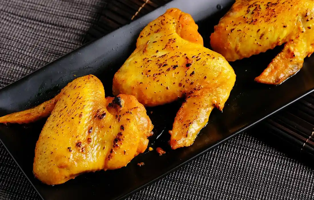 Golden roasted chicken wings arranged on a black rectangular plate.