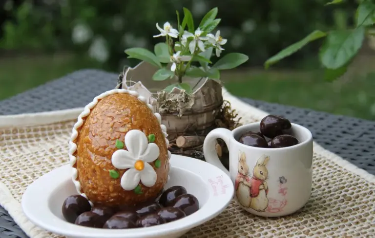 Tabletop garden scene with a flower-decorated pastry on a plate, a rabbit-themed mug, and a potted flowering plant in the background.