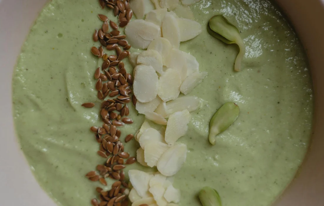 Green creamy mixture topped with flax seeds, almond slices, and cucumber slices