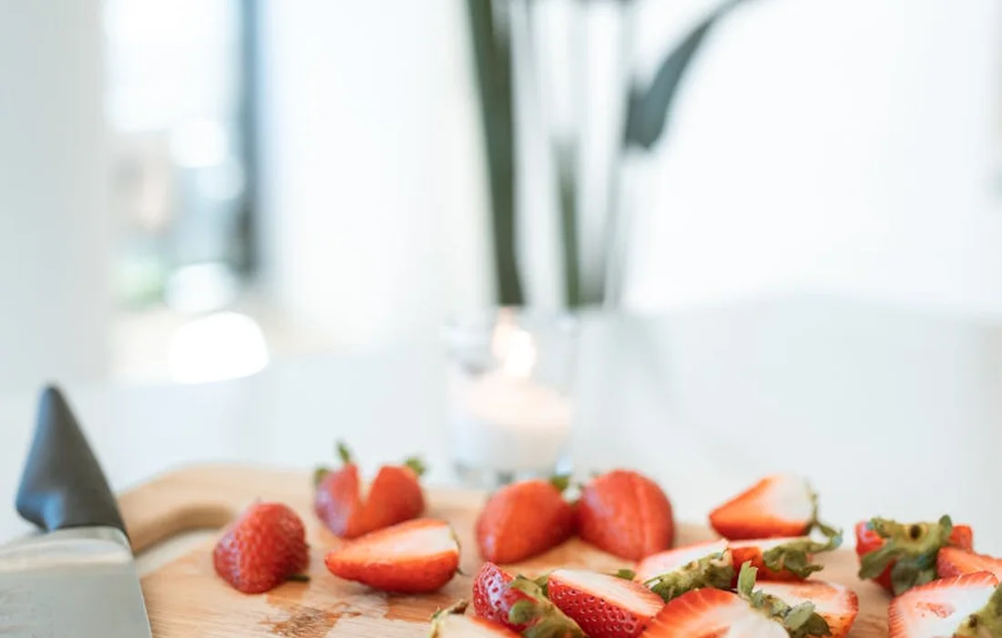 Fresh strawberries sliced and whole on a wooden surface, ready as treats for backyard chickens.
