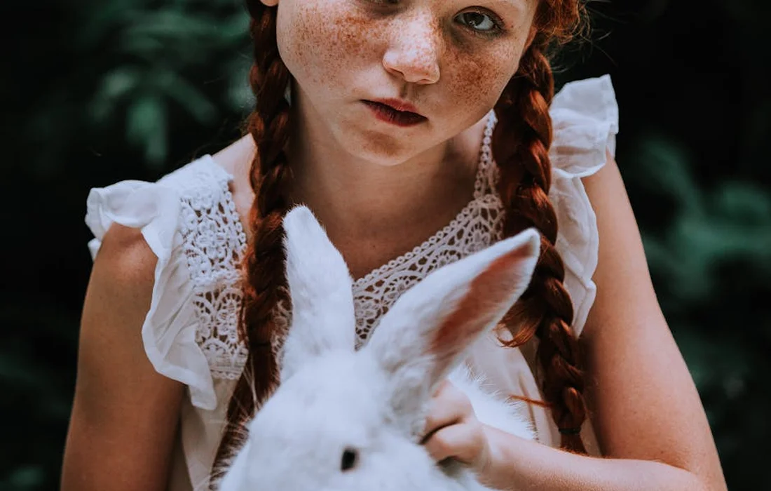 Close-up of a young girl with braids holding a white rabbit outdoors