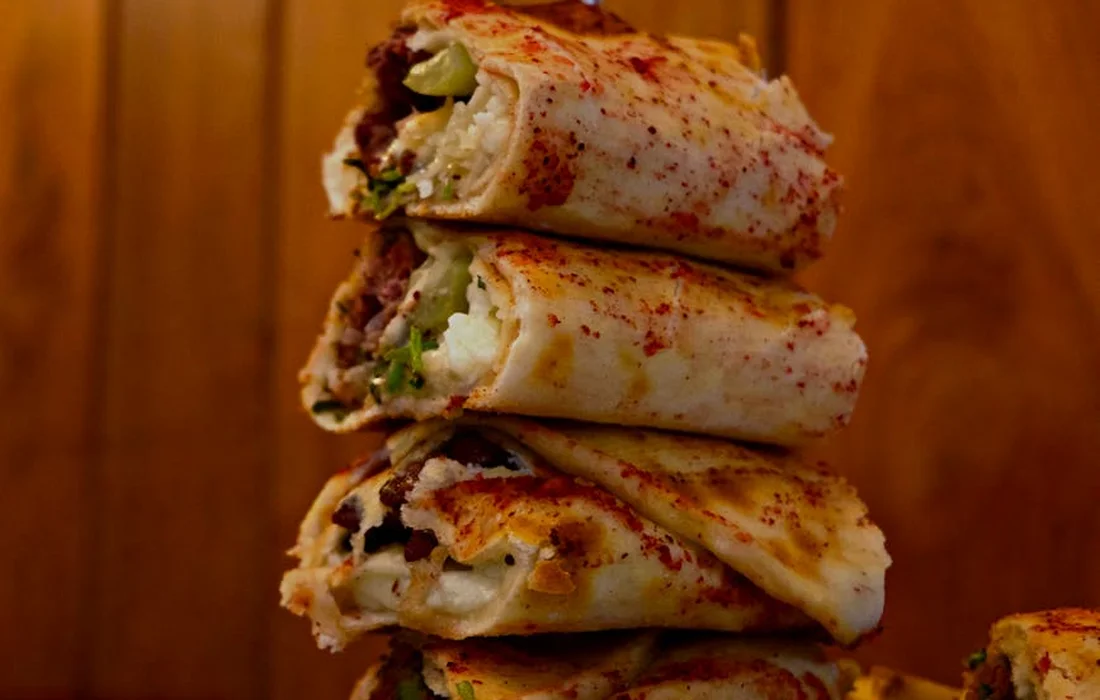 Stacked herb-seasoned wraps with greens and a dusting of red spice.