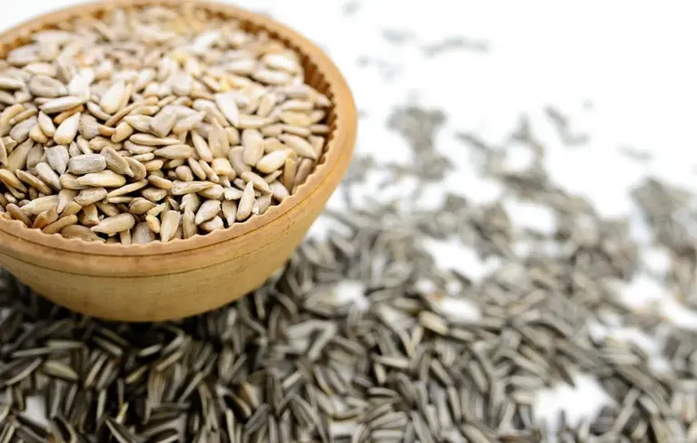 Wooden bowl filled with sunflower seeds, with seeds spilled onto a white surface