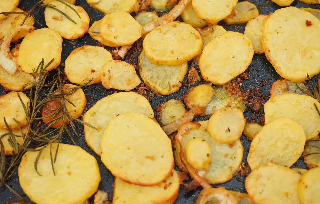 Close-up of round sliced sweet potatoes roasted on a dark baking sheet with a sprig of rosemary