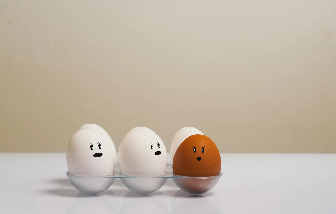 Three eggs in egg cups with drawn faces on a white surface against a pale background.