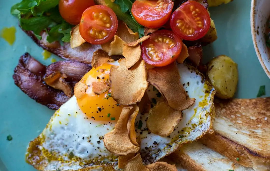 Close-up of a plate with halved cherry tomatoes and a fried egg topped with crispy chips