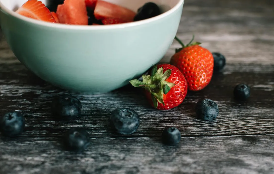 Turquoise bowl filled with sliced strawberries and blueberries on a dark, weathered wooden surface.