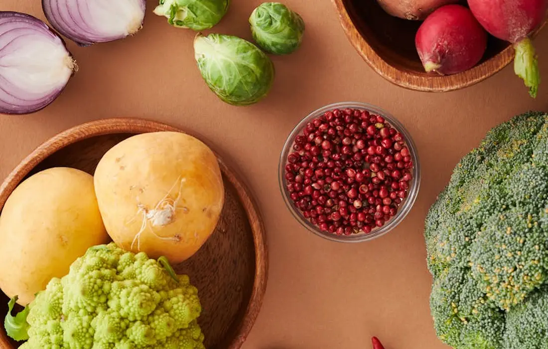 Assorted fresh vegetables on a wooden table, including broccoli, cauliflower, onions, and red radishes