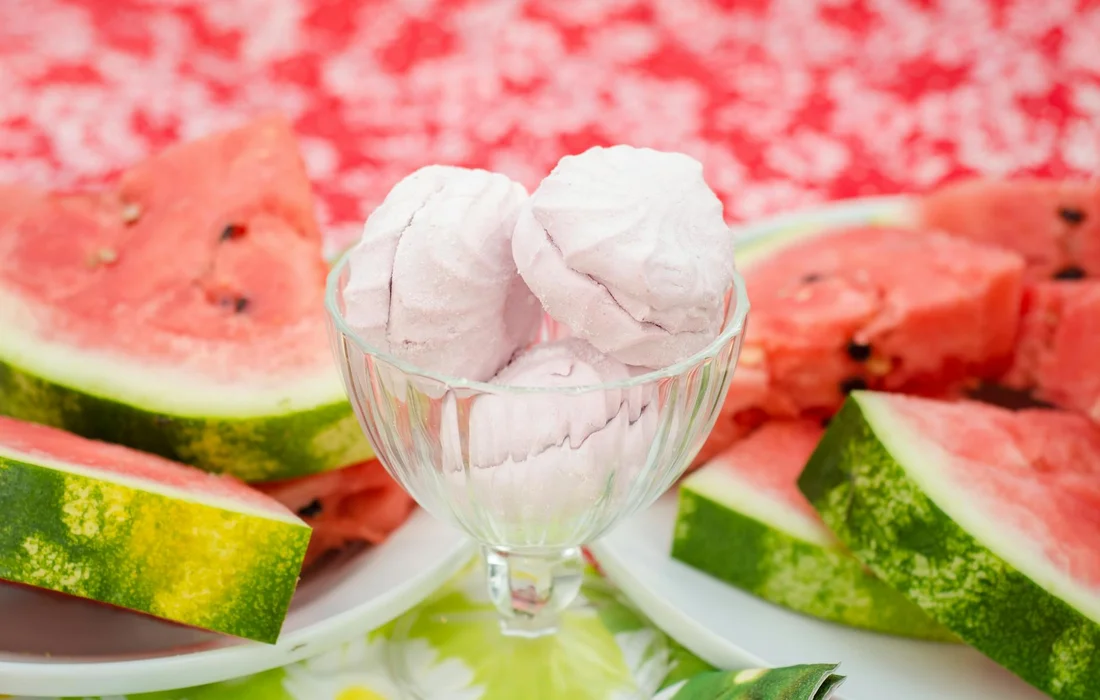 Slices of watermelon arranged on plates around a clear glass dessert cup filled with white spherical items.